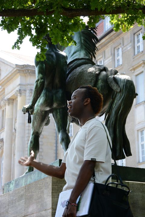 Tour guide speaking in front of a colonial-era statue in Berlin